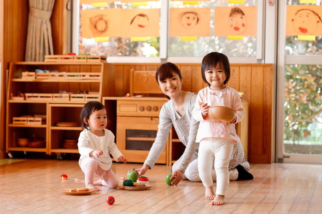 A caregiver playing with two toddlers at a toy kitchen in a child care program