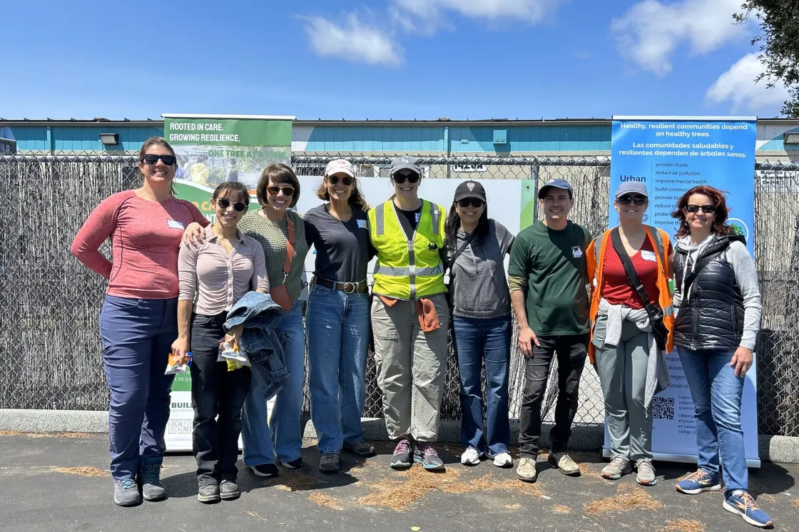 Volunteers gathered under a Rooted in Care — Growing Resilience banner at a community tree planting